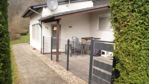 A building with a paved entrance, a fenced patio area with outdoor furniture, and a number '36' on the wall. - Ferienhaus am Stausee Bitburg (Biersdorf am See)