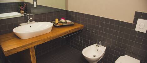 Un baño moderno con tocador de madera, lavamanos blanco, un bidé y un inodoro.