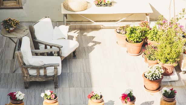 Een terras met een houten stoel en een tafel, omringd door potplanten en bloemen.