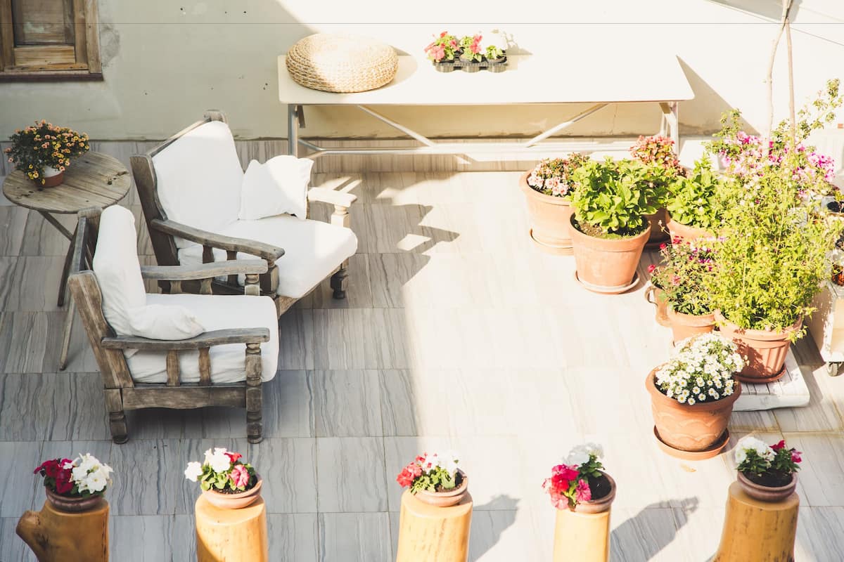 Un espace patio avec une chaise en bois et une table, entouré de plantes et de fleurs en pot.