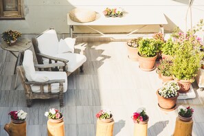 Un patio con una silla y una mesa de madera, rodeado de plantas y flores en macetas.