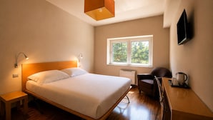 Een slaapkamer met een bed, nachtkastjes, een bureau met stoel, een raam met uitzicht en een wandtelevisie.