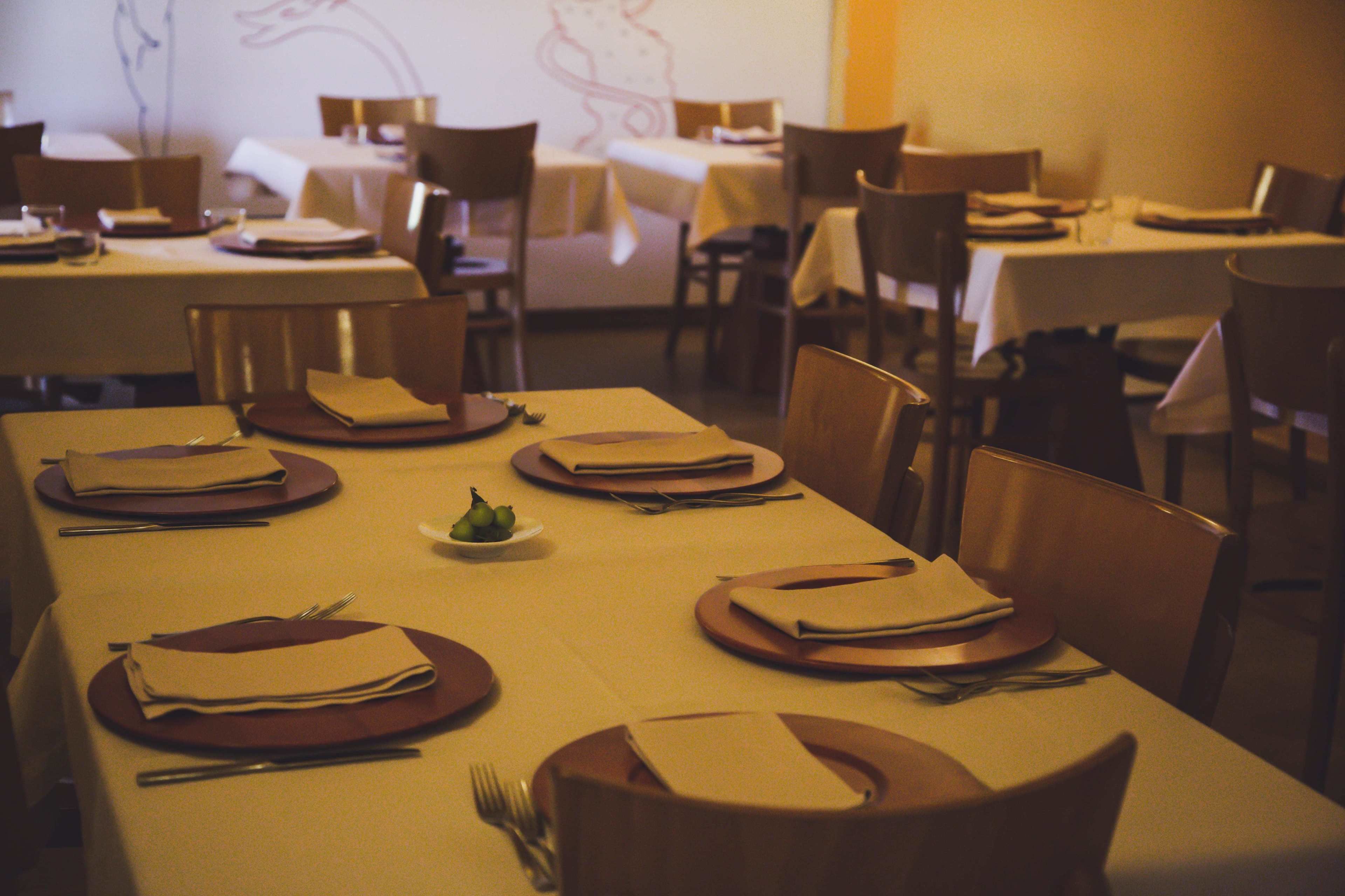 Un restaurante con mesas dispuestas para comer, sillas y un tazón pequeño de fruta sobre la mesa.