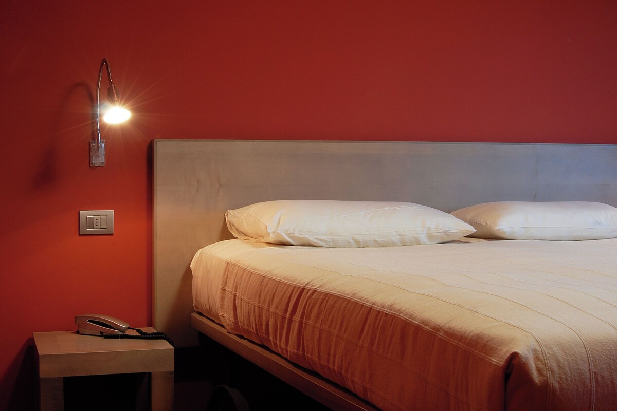 Ein Schlafzimmer mit Bett, Nachttisch, Lampe und einer Steckdose.