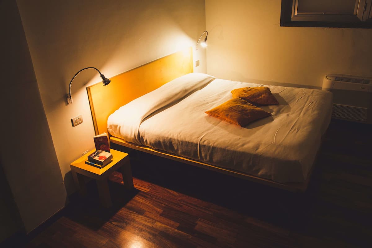 Un lit bien fait, avec une tête de lit, une table de chevet avec une lampe et une petite table de nuit sur laquelle repose un livre.