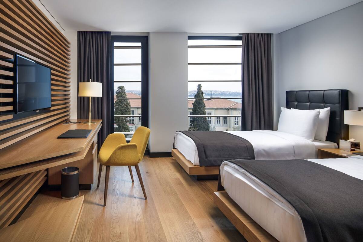Hotellihuone, jossa on työpöytä, kaksi sänkyä, televisio ja näkymä rakennuksiin.