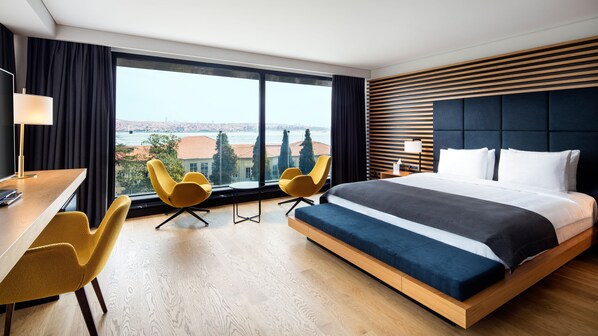 A modern hotel room with a large bed, two yellow chairs, a desk, and a view of the city. - Metropolitan Hotels Bosphorus (Istanbul)