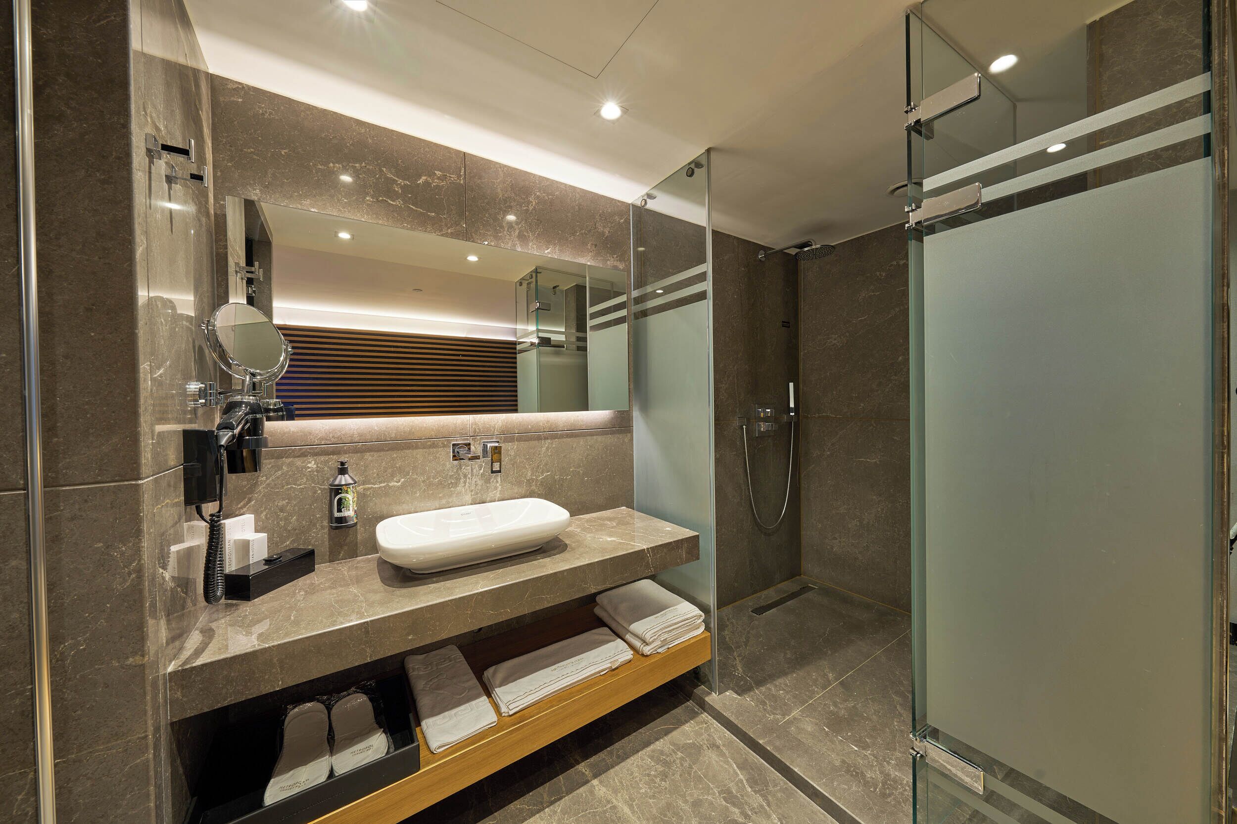 A modern bathroom with a large mirror, a sink, a shower, and a glass-enclosed shower stall.
