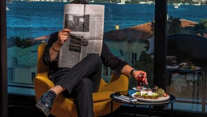 A person sitting by a window with a newspaper, overlooking a cityscape and water. - Metropolitan Hotels Bosphorus (Istanbul)
