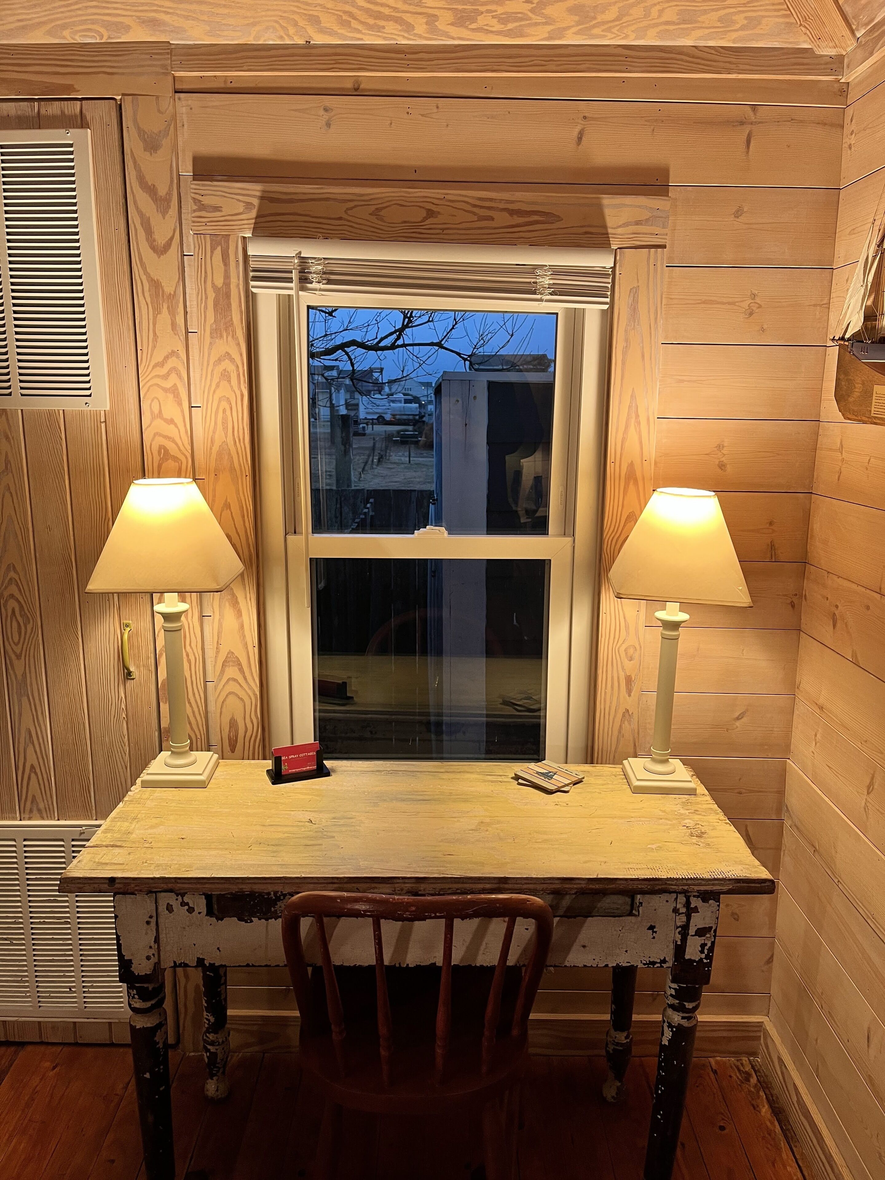 En træhytte med et vindue, to lamper, et lille bord og en stol.