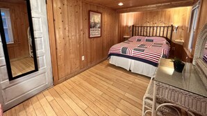Un dormitorio con paneles de madera, una cama, una mesita de vidrio y una silla de mimbre.