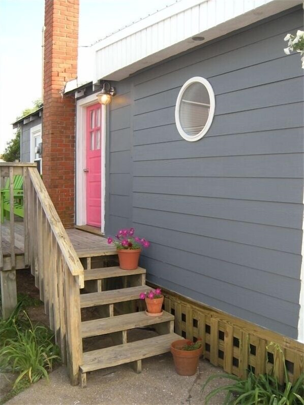 A house with a wooden staircase leading to a pink door, grey siding, and a small window.