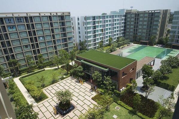 A modern building complex with multiple high-rise structures, a central courtyard with a green lawn, and a small brick building with a green roof.