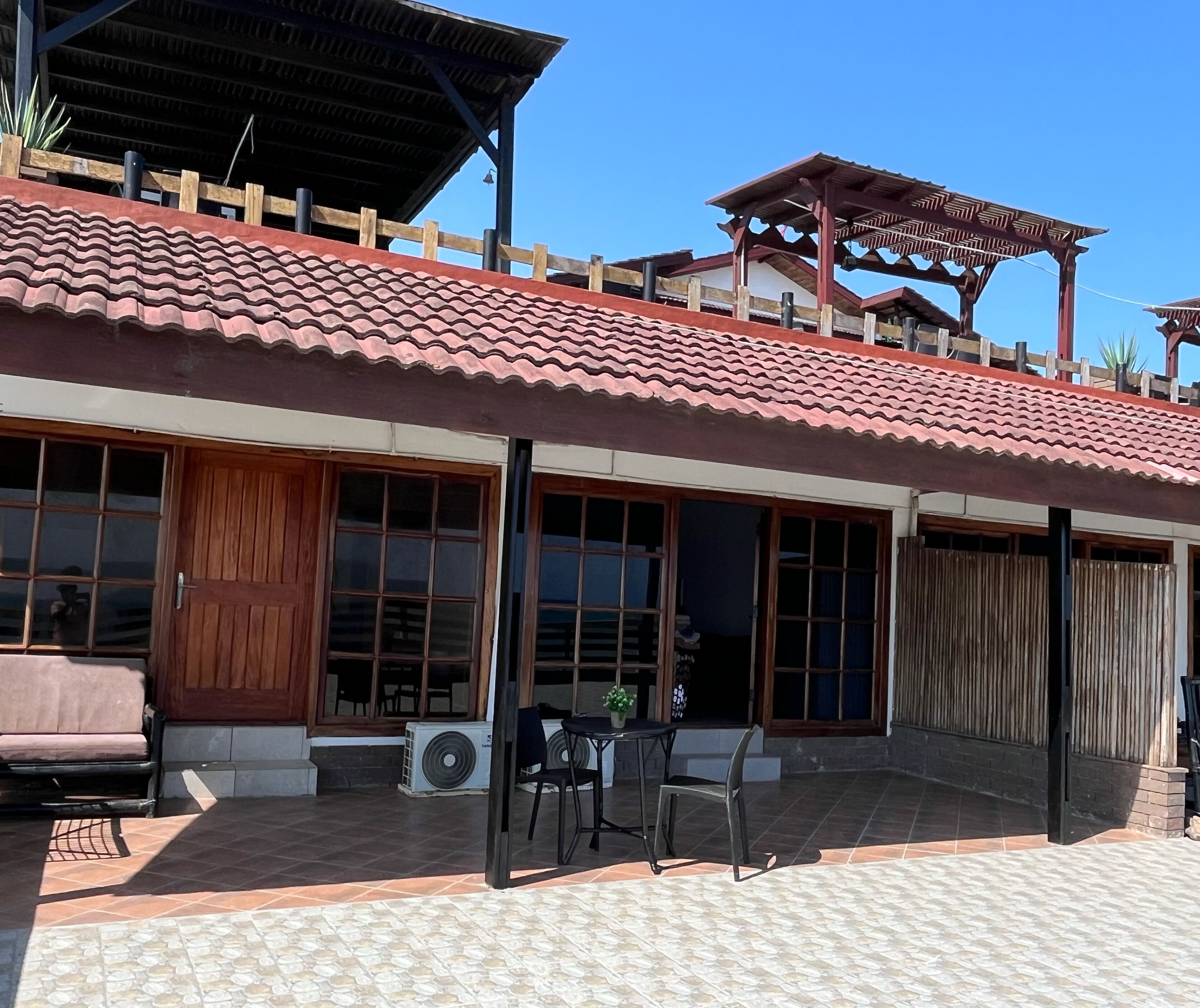 A two-story building with a tiled roof, large windows, and a covered patio area with outdoor furniture.