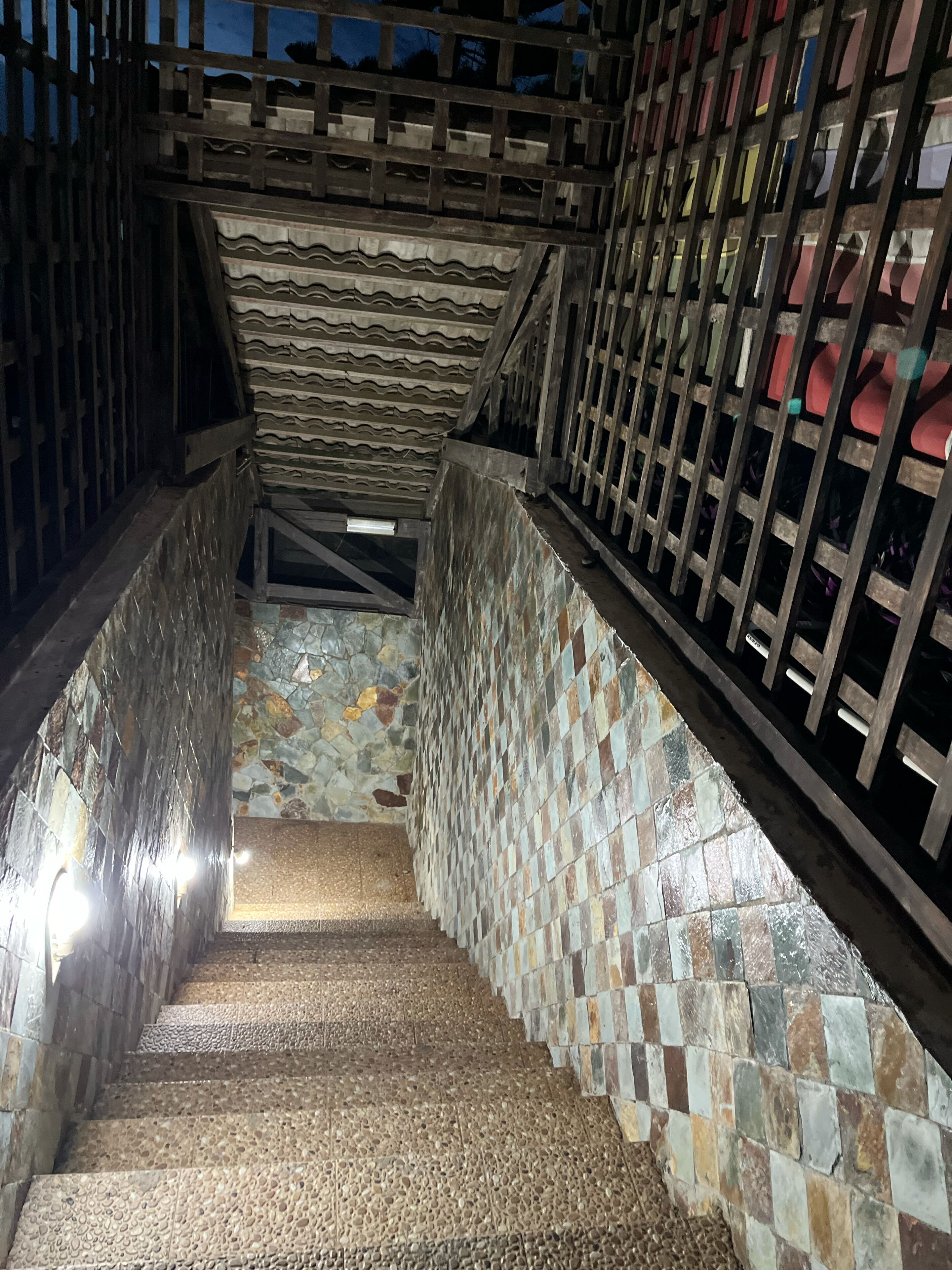 A staircase with stone steps and a tiled wall, enclosed by metal railings.