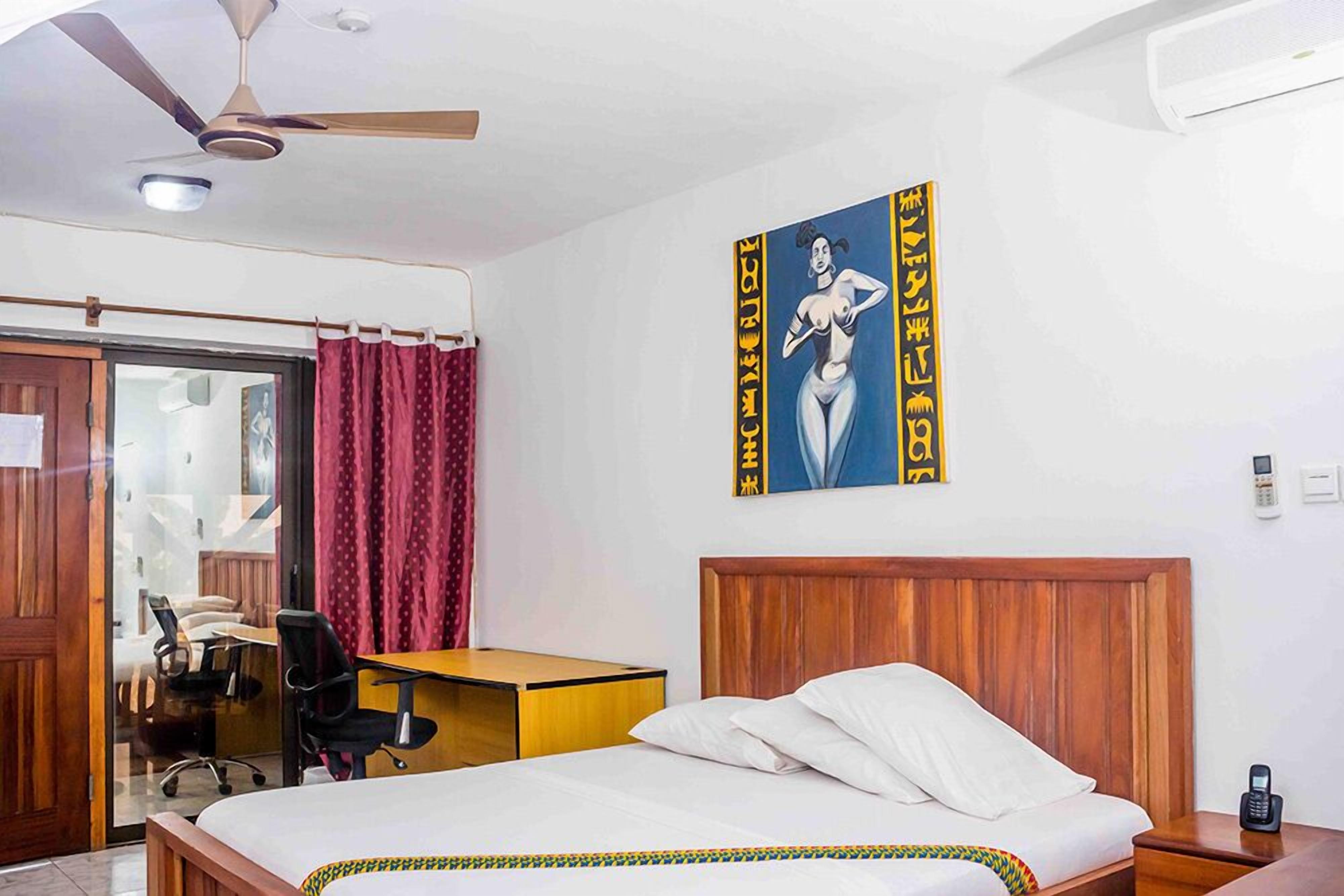 A hotel room with a wooden bed, a desk, a chair, and a ceiling fan.