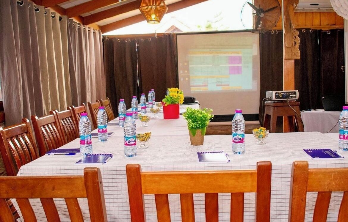 A conference room with a long table, chairs, water bottles, a projector screen, and a small plant.
