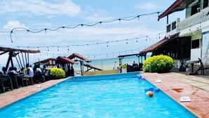 A swimming pool with a person swimming, surrounded by a covered area with string lights. - Veivaag Lodge (Sekondi-Takoradi)