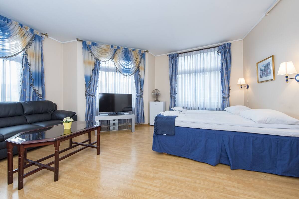 A hotel room with a bed, a sofa, a TV, a desk, and a lamp.