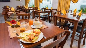 A dining area with wooden tables and chairs, a breakfast setting with toast, eggs, and juice, and yellow napkins. - Stavanger Lille Hotel (Stavanger)