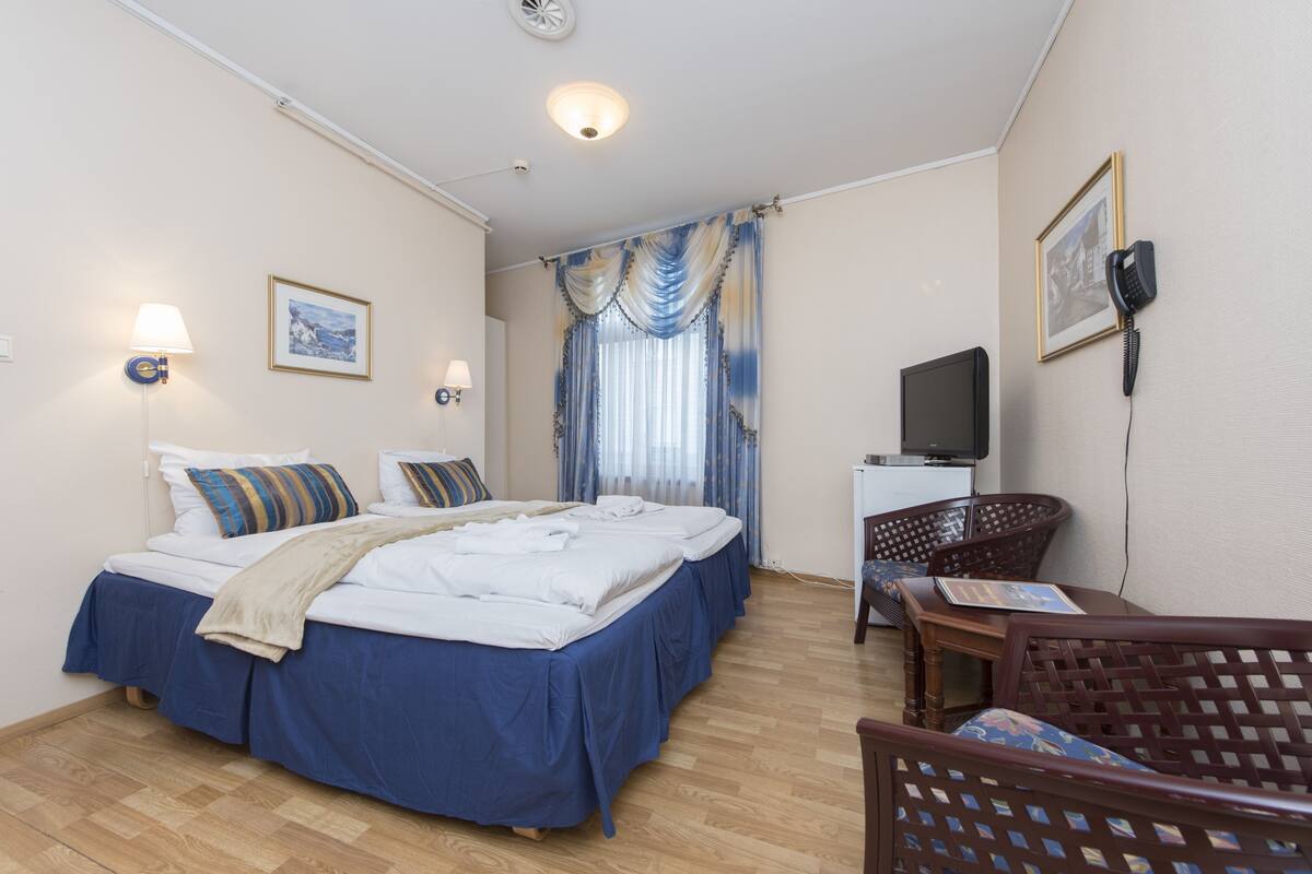 A hotel room with a bed, two bedside lamps, a desk with a chair, a television, and a telephone on the wall.