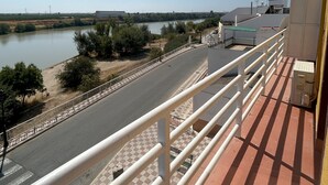 A balcony with a view of a river, a road, and some greenery.