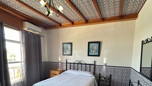 A room with a checkered floor, a bed with a white bedspread, a ceiling with a star pattern, and two framed pictures on the wall.