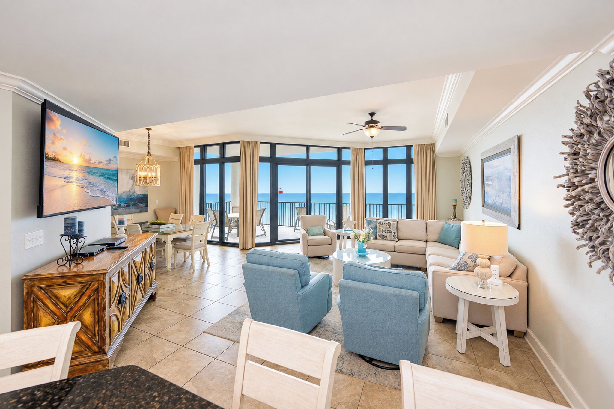 A spacious living area with a large window overlooking the ocean, a dining area with a view, and a balcony with a ceiling fan.