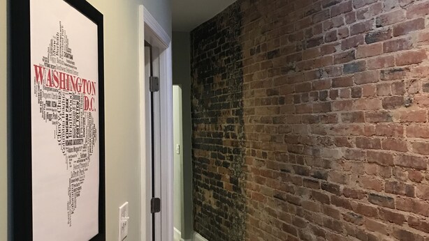 Un couloir avec un mur en briques, une carte encadrée de Washington D.C. et une lucarne.