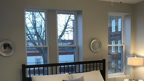 Une chambre à coucher comprenant un lit, un ventilateur de plafond, deux fenêtres, une table de chevet et un miroir fixé au mur.