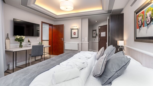 Une chambre d’hôtel moderne dotée d’un grand lit, d’un bureau avec une chaise, d’un téléviseur à écran plat et d’une salle de bain visible à travers une porte ouverte.