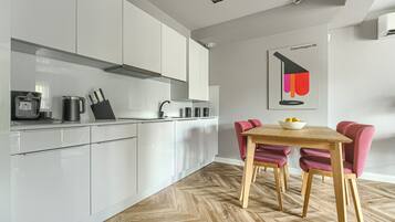 Una cocina moderna con armarios blancos, suelo de madera en espiga y un comedor con mesa de madera y sillas rojas.