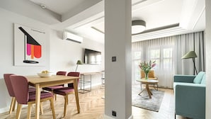 Un salon moderne avec un coin repas, comprenant un parquet en bois disposé en chevrons, un canapé de couleur turquoise et une table à manger avec des chaises.