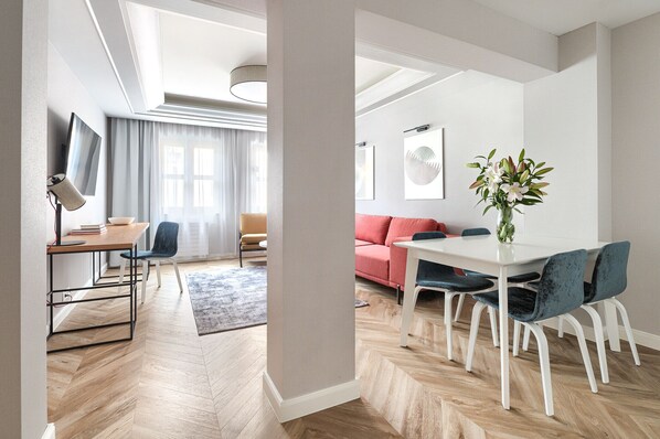 A modern living room with a dining area, a sofa, a TV, and a vase of flowers.