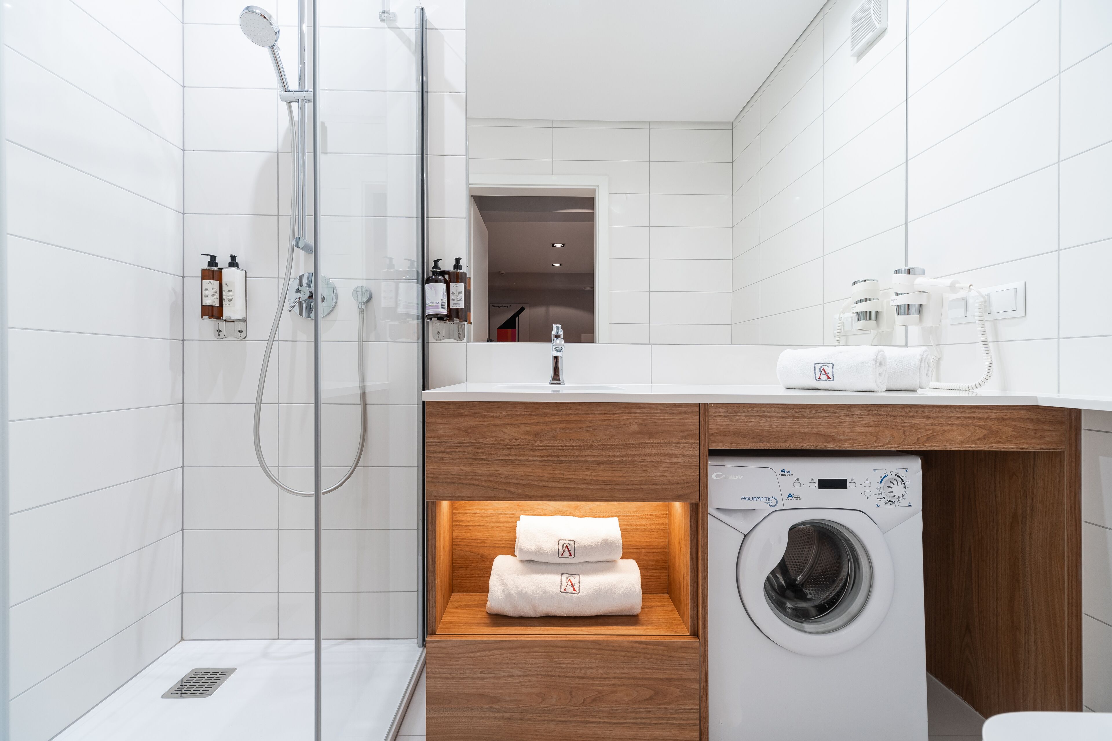 A modern bathroom with a glass-enclosed shower, a wooden vanity with a built-in washing machine, and neatly folded towels.