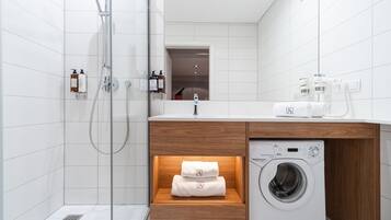 A modern bathroom with a glass-enclosed shower, a wooden vanity with a built-in washing machine, and neatly folded towels.