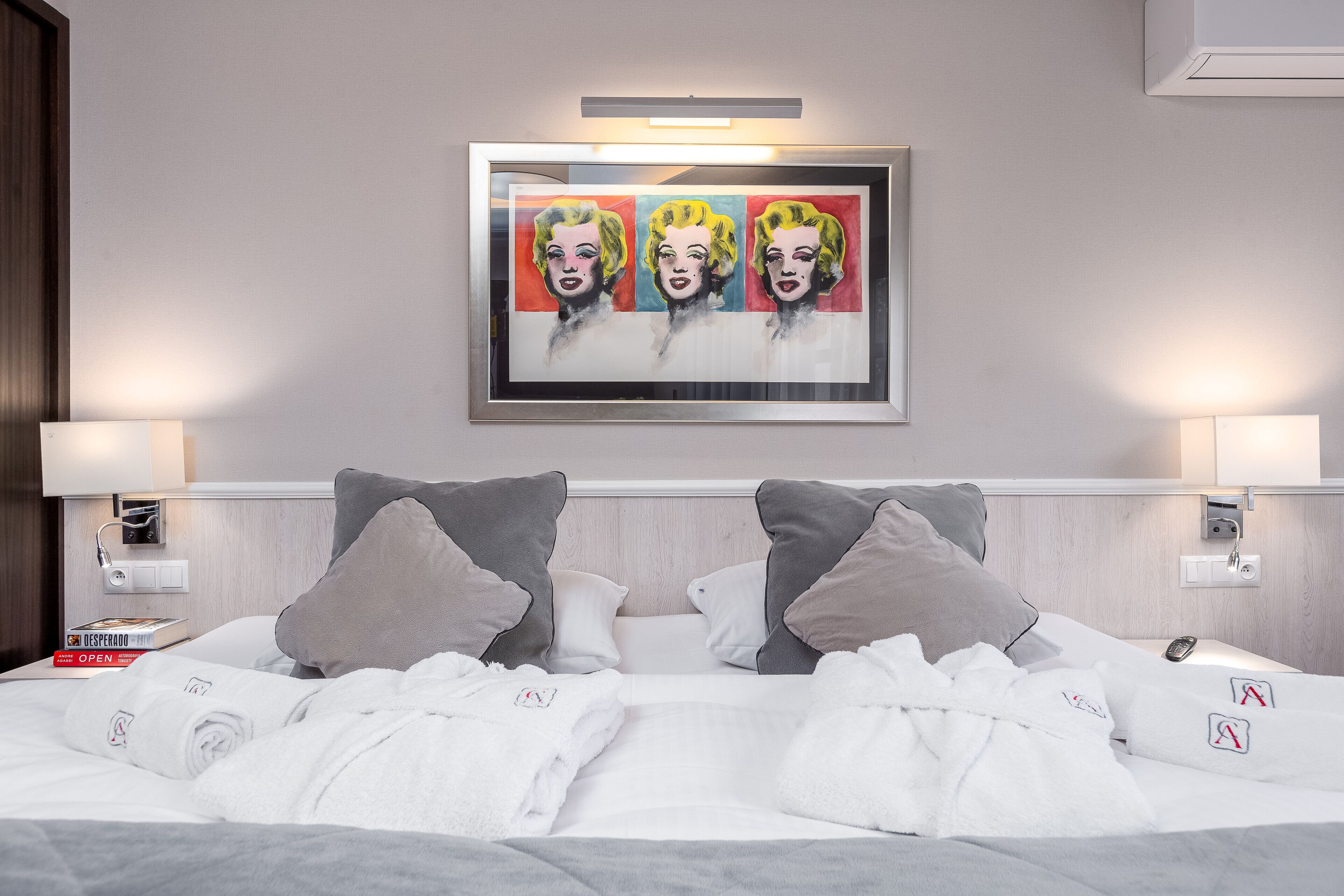 Habitación de hotel con cama, almohadas, una obra de arte enmarcada, lámparas de noche y un libro sobre la mesita.