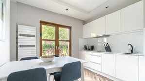 Une cuisine moderne avec des meubles blancs, une table à manger avec des chaises et une fenêtre donnant sur un paysage verdoyant.