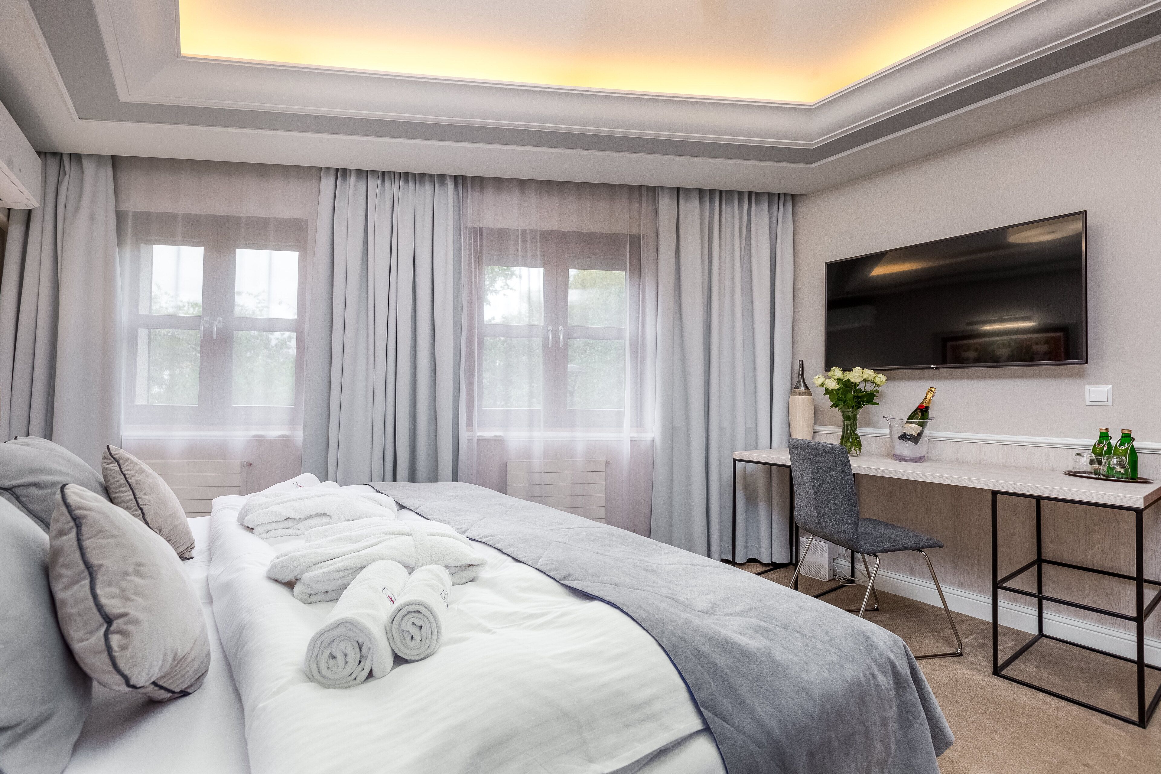 Una habitación de hotel moderna con una cama bien hecha, un escritorio con silla, un televisor de pantalla plana y un ventanal con cortinas.