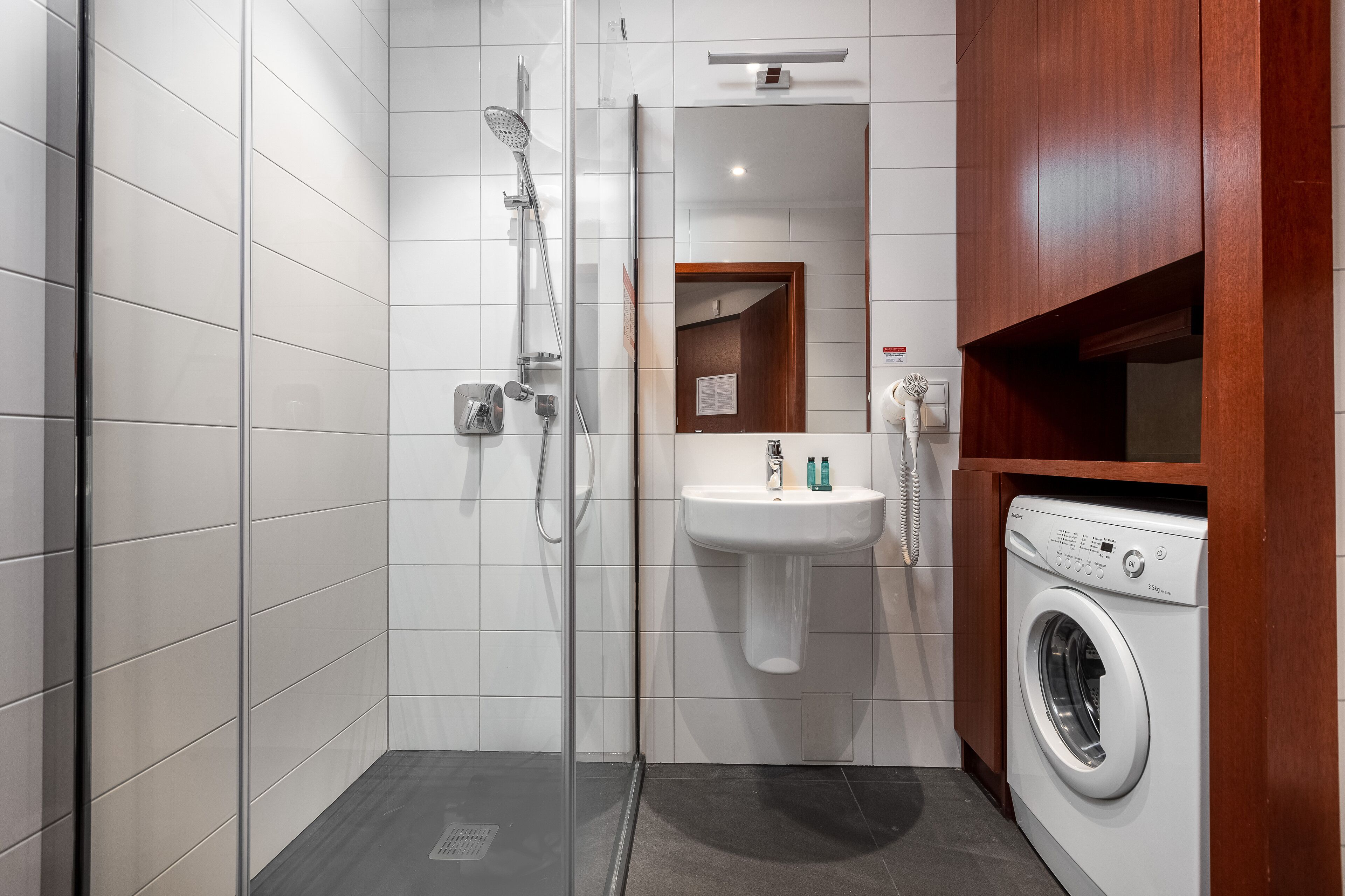 A modern bathroom with a glass shower enclosure, a white sink, and a built-in washing machine.