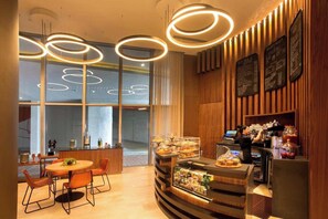 Una cafetería moderna con interior de madera, una mesa redonda con sillas, una barra con vitrina y carteles con el menú.