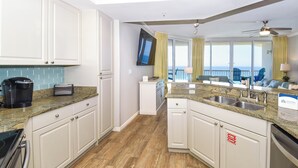 A modern kitchen with granite countertops, white cabinetry, and a view to the balcony. - Hardwood flooring throughout updated, tropical condo! 🌺 (Destin)
