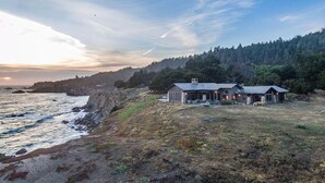 A coastal property with a house near the water, surrounded by forested hills. - Private, Oceanfront Views, Starlink WiFi, Timber Cove (Jenner)