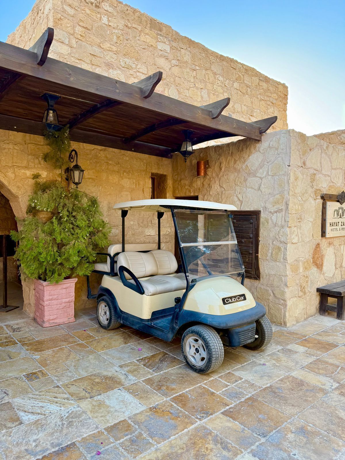 A golf cart parked in front of a stone building with a wooden pergola overhead.
