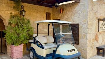 A golf cart parked in front of a stone building with a wooden pergola overhead.