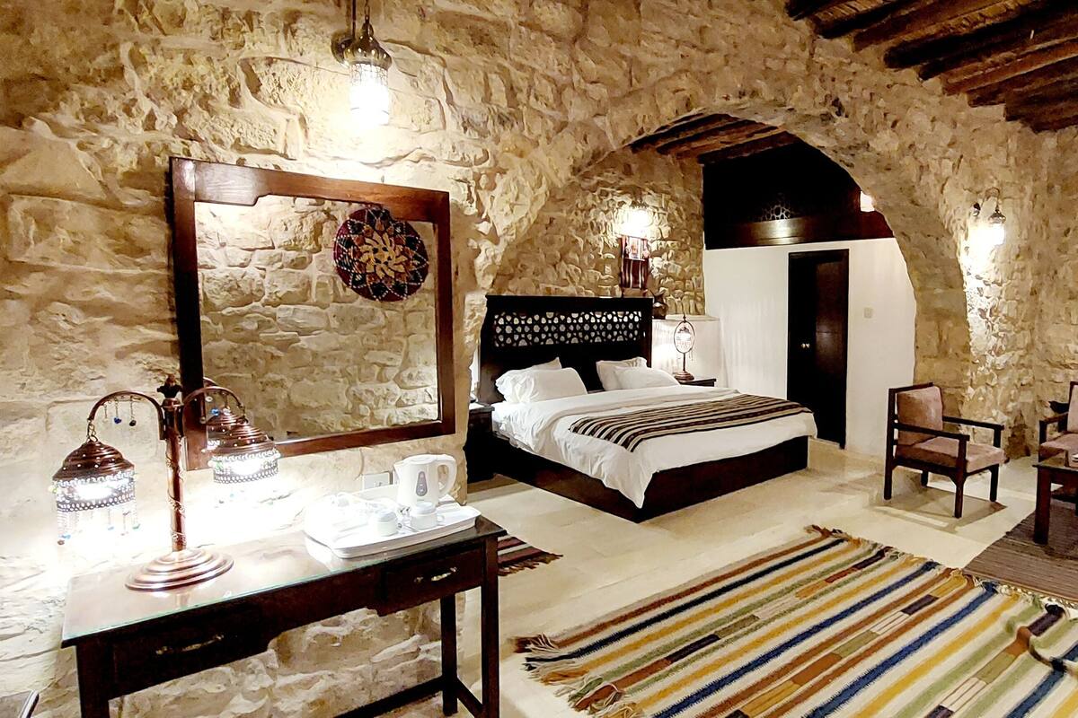 Une chambre à coucher rustique avec un mur en pierre, un lit en bois, un bureau avec une lampe, une chaise et une petite table.