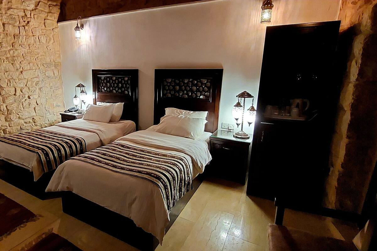 Une chambre avec deux lits, des murs en pierre, un plafond en bois et un petit tapis.
