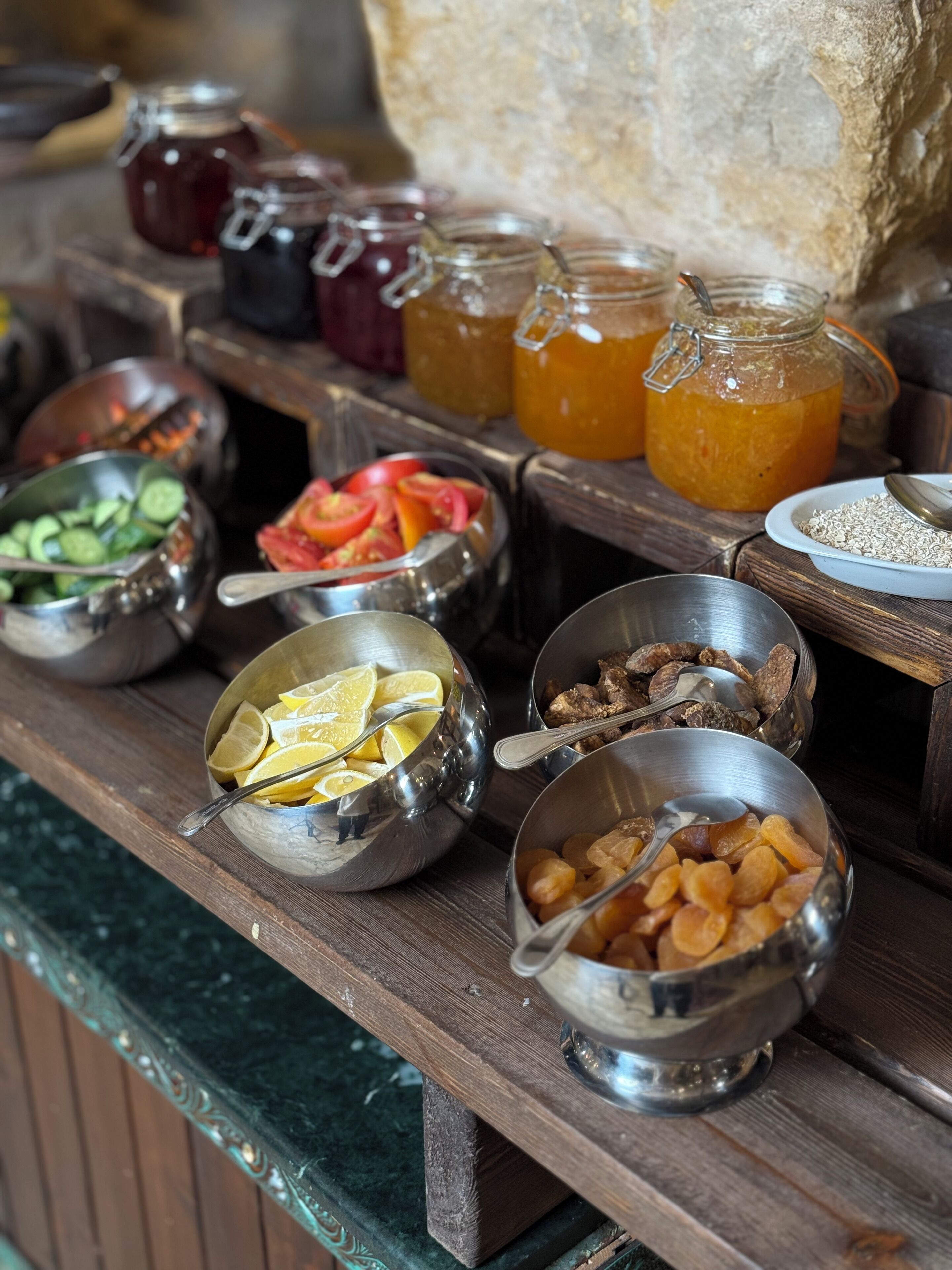 Un bufé con diversos alimentos en recipientes metálicos, entre ellos frutas, verduras y salsas.