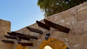A stone archway structure with wooden beams and lanterns, leading to an outdoor area with tiled flooring and benches. - Hayat Zaman Hotel & Resort (At-Taybeh)