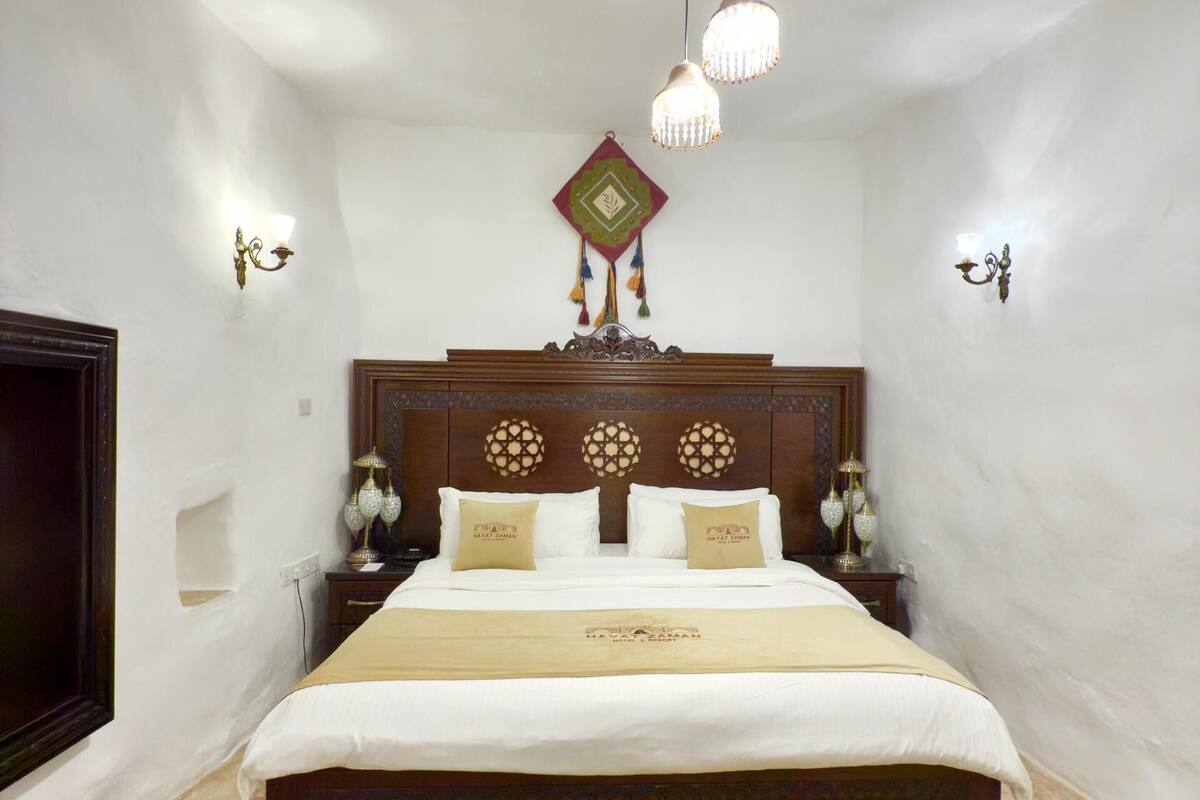 Une chambre à coucher bien aménagée, avec un grand lit, une tête de lit décorative, des lampes fixées au mur et un tapis à motifs.